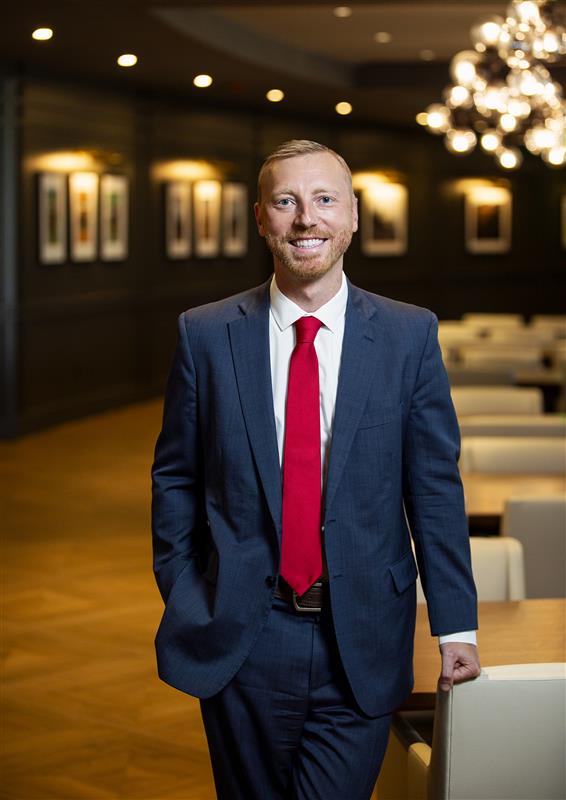 Professional man in a suit and red tie standing confidently in a modern office setting, representing Alex White, PLLC, a personal injury law firm.
